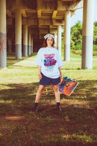 a woman wearing a white t - shirt standing under a bridge