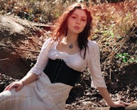 a woman in a white dress sitting on a log in the woods